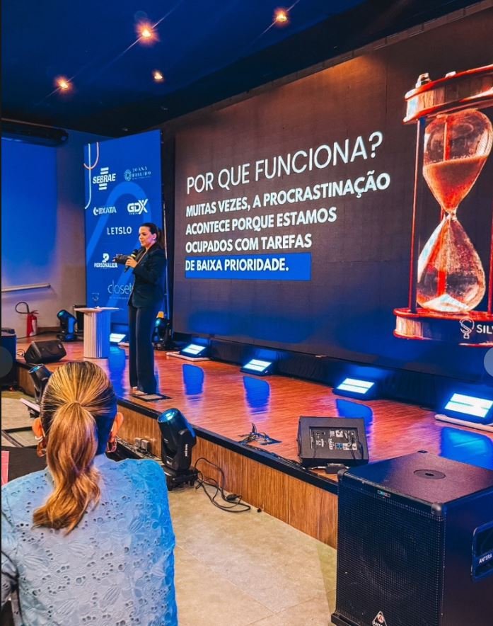 Palestrante em evento corporativo diante de painel de LED com a pergunta “Por que funciona?”, com monitores de retorno e iluminação azul montados pela GDX Brasil.