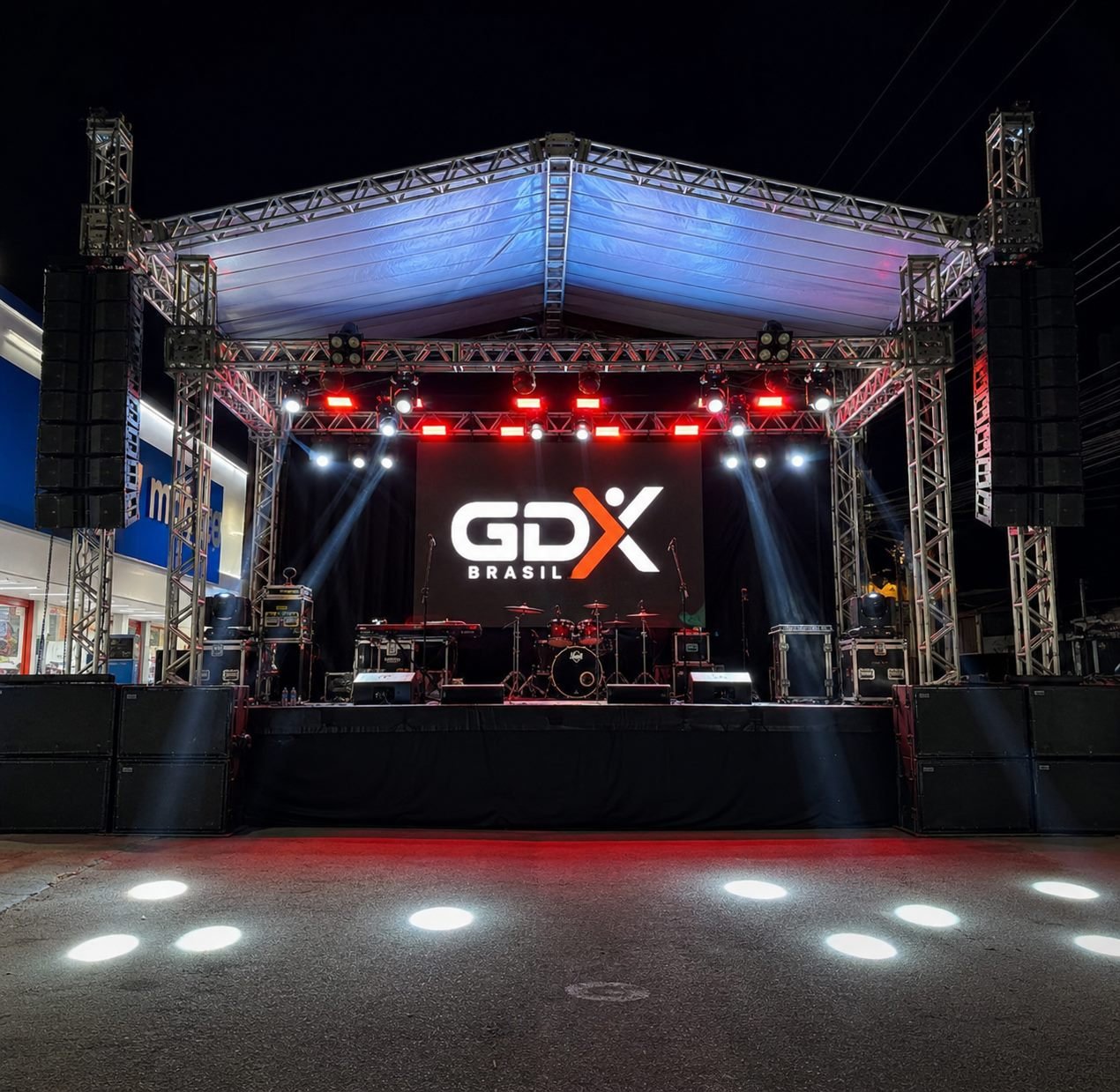 Palco de evento à noite montado pela GDX Brasil, com painel de LED exibindo o logo GDX, treliças de estrutura, line arrays de som e iluminação cênica.